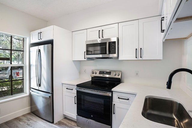 kitchen with light hardwood / wood-style floors, light stone counters, white cabinets, stainless steel appliances, and sink