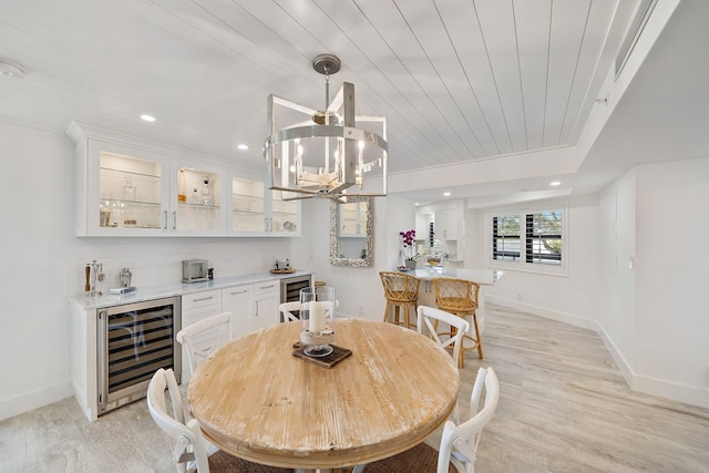 dining area featuring an inviting chandelier, beverage cooler, light hardwood / wood-style floors, and indoor bar