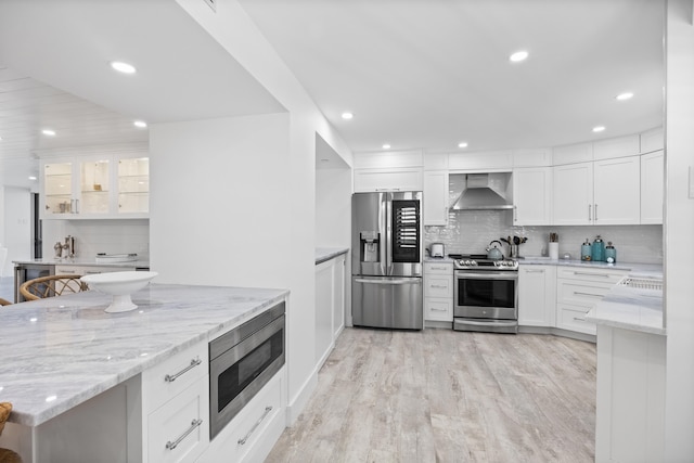 kitchen with light hardwood / wood-style floors, tasteful backsplash, white cabinetry, wall chimney exhaust hood, and appliances with stainless steel finishes