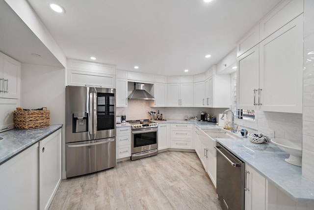 kitchen with sink, wall chimney exhaust hood, light hardwood / wood-style flooring, white cabinetry, and stainless steel appliances