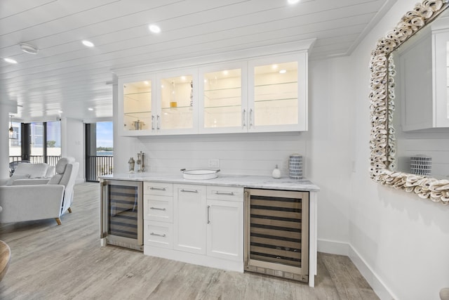 bar featuring light wood-type flooring, light stone countertops, beverage cooler, and white cabinets