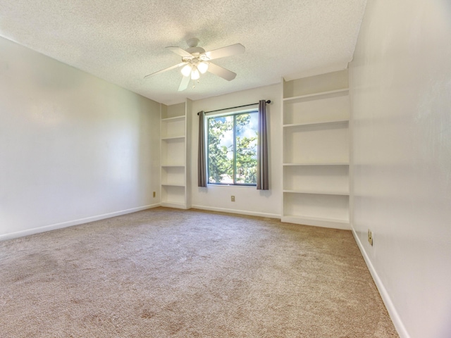 spare room with ceiling fan, a textured ceiling, built in shelves, and carpet