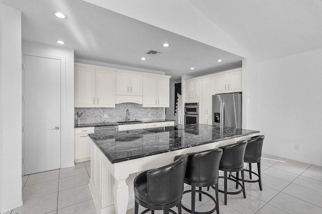 kitchen featuring sink, dark stone countertops, a kitchen island, stainless steel appliances, and light tile patterned flooring