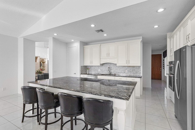 kitchen featuring light tile patterned flooring, dark stone countertops, stainless steel refrigerator, a kitchen island, and white cabinets