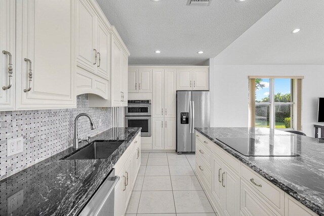 kitchen with white cabinets, a center island, dark stone countertops, decorative backsplash, and stainless steel refrigerator