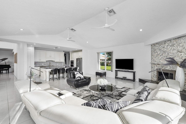 living room featuring a textured ceiling, lofted ceiling, a fireplace, light tile patterned flooring, and ceiling fan