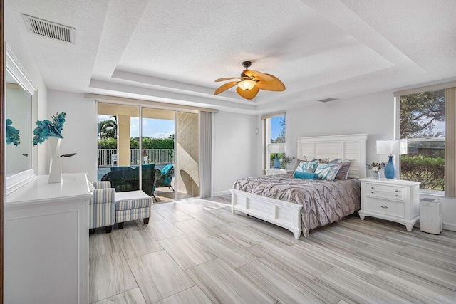 bedroom with ceiling fan, access to exterior, and a tray ceiling