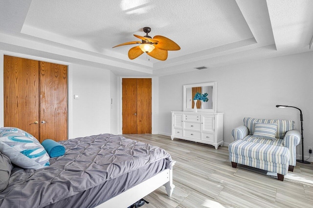 bedroom with a raised ceiling, ceiling fan, and a textured ceiling