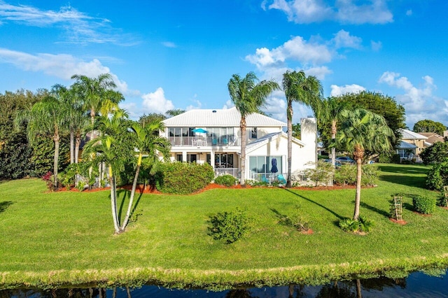 back of house with a balcony, a lawn, and a water view