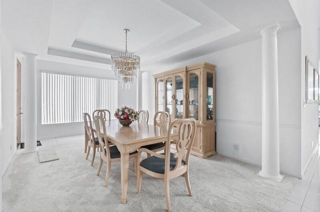 carpeted dining room featuring a raised ceiling, a notable chandelier, and decorative columns