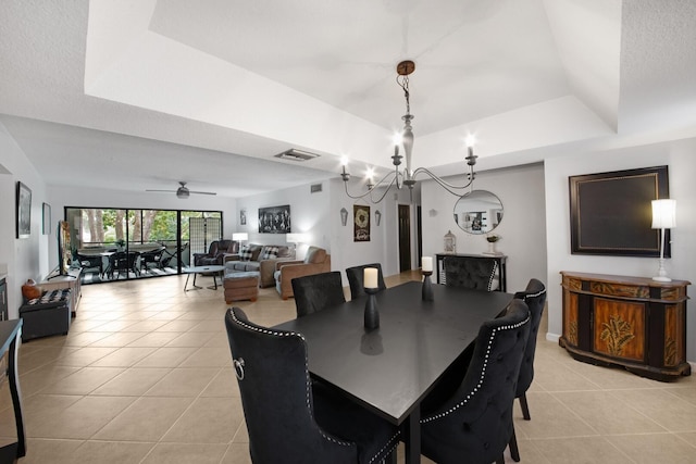 tiled dining area featuring a textured ceiling, ceiling fan with notable chandelier, and a tray ceiling