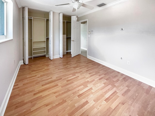 unfurnished bedroom featuring crown molding, light hardwood / wood-style floors, two closets, and ceiling fan