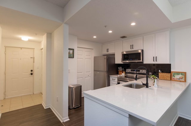 kitchen with white cabinetry, kitchen peninsula, stainless steel appliances, backsplash, and dark hardwood / wood-style flooring