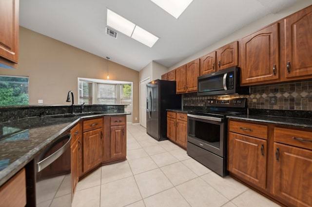 kitchen featuring lofted ceiling with skylight, sink, dark stone countertops, stainless steel appliances, and decorative backsplash