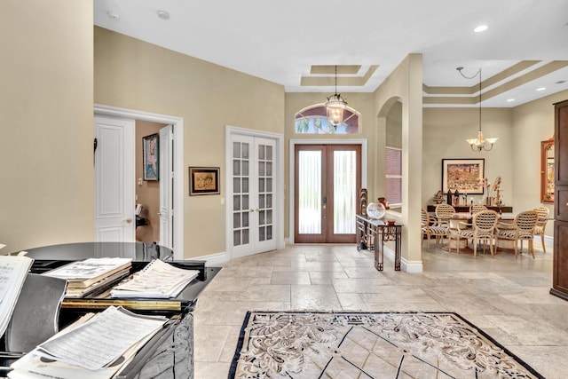 foyer entrance with a notable chandelier, a raised ceiling, and french doors