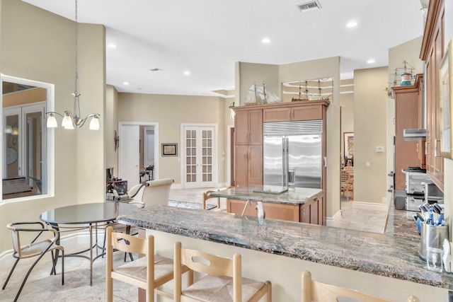 kitchen with kitchen peninsula, french doors, light stone counters, pendant lighting, and stainless steel built in fridge