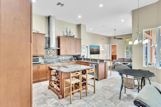 kitchen featuring ceiling fan, wall chimney range hood, stone countertops, dishwasher, and a kitchen island