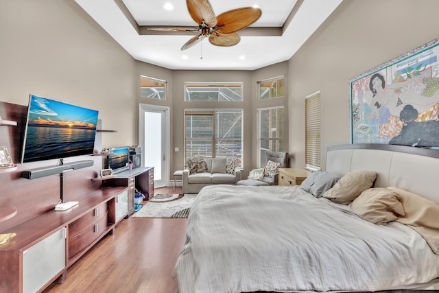 bedroom with a tray ceiling, ceiling fan, light hardwood / wood-style flooring, and a high ceiling