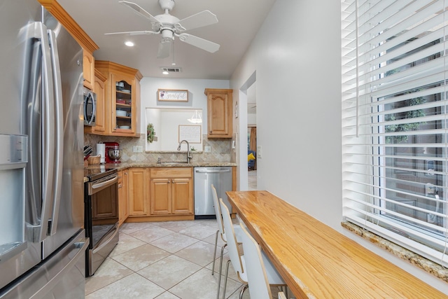 kitchen with sink, stainless steel appliances, light stone counters, decorative backsplash, and light tile patterned floors