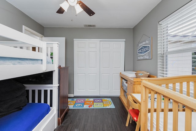 bedroom with ceiling fan, dark wood-type flooring, a nursery area, and a closet