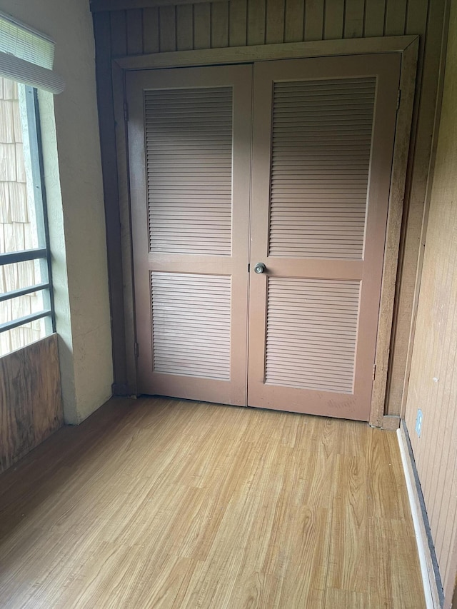 unfurnished bedroom with wooden walls, light hardwood / wood-style floors, and multiple windows