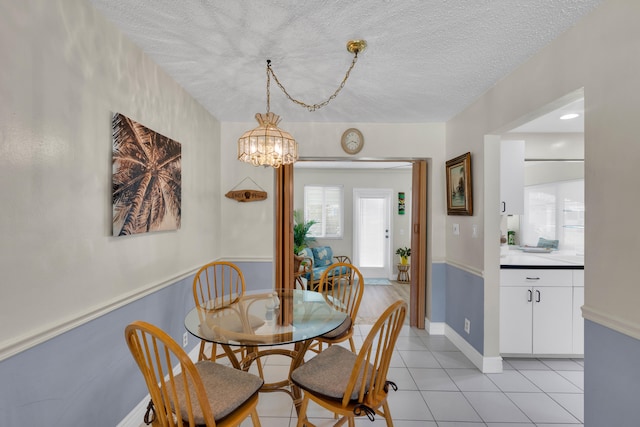 dining area with an inviting chandelier, a textured ceiling, and light tile patterned floors