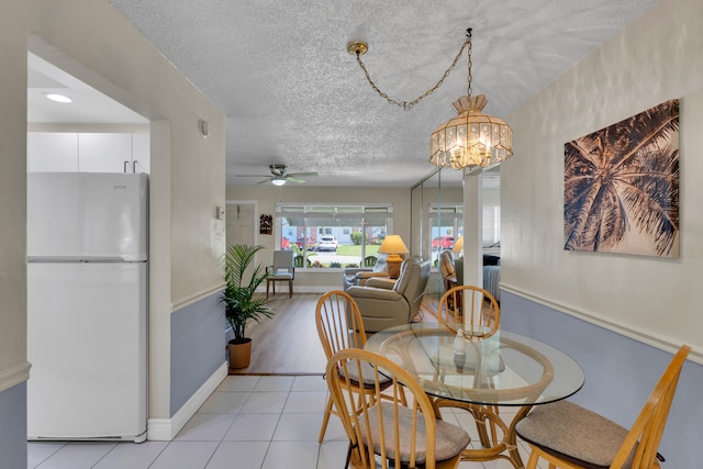 dining room featuring a textured ceiling, ceiling fan with notable chandelier, and light tile patterned flooring