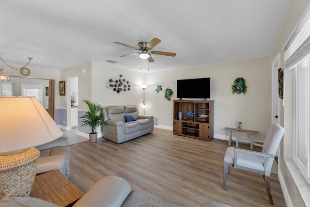 living room featuring a textured ceiling, ceiling fan with notable chandelier, and light hardwood / wood-style floors