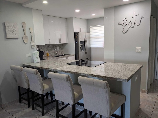 kitchen featuring white cabinets, a breakfast bar area, stainless steel fridge, and kitchen peninsula