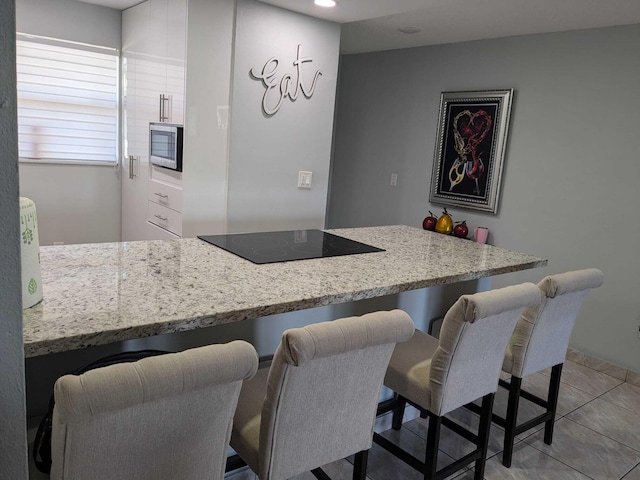 kitchen with a kitchen breakfast bar, black electric stovetop, stainless steel microwave, and light tile patterned flooring