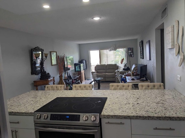 kitchen featuring light stone counters, stainless steel range with electric stovetop, and white cabinetry