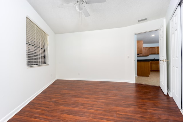 empty room featuring a textured ceiling, ceiling fan, and dark wood-type flooring