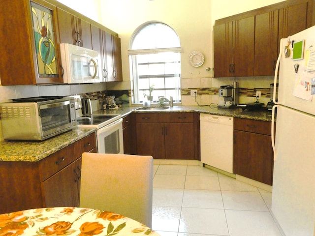 kitchen with dark stone counters, white appliances, sink, and tasteful backsplash