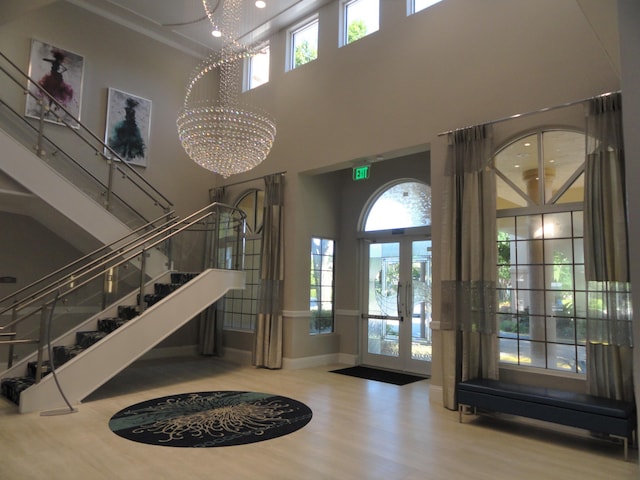 entryway featuring wood-type flooring, a towering ceiling, french doors, and a notable chandelier