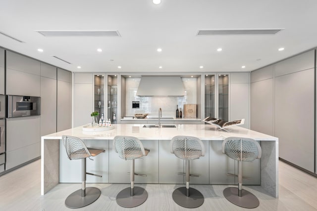 kitchen featuring a large island, a breakfast bar, sink, and premium range hood