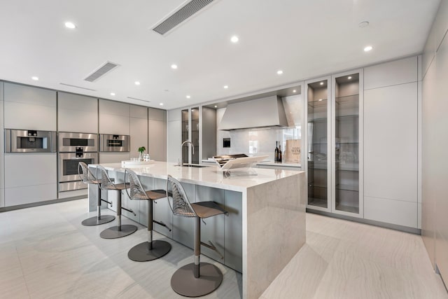 kitchen with gray cabinetry, a breakfast bar area, premium range hood, a large island, and sink