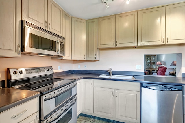 kitchen with track lighting, appliances with stainless steel finishes, cream cabinetry, and sink