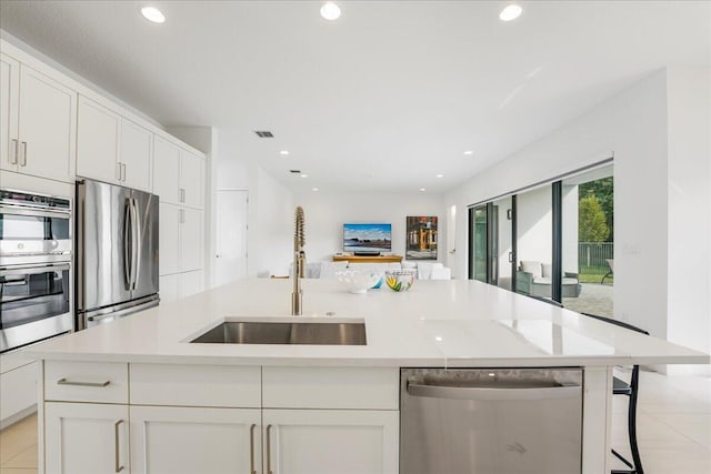 kitchen with an island with sink, appliances with stainless steel finishes, sink, and white cabinets