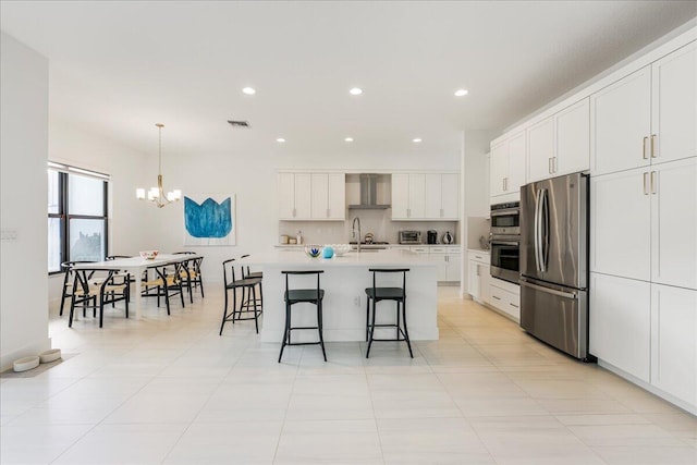 kitchen with white cabinetry, stainless steel fridge, a kitchen breakfast bar, a center island with sink, and wall chimney exhaust hood