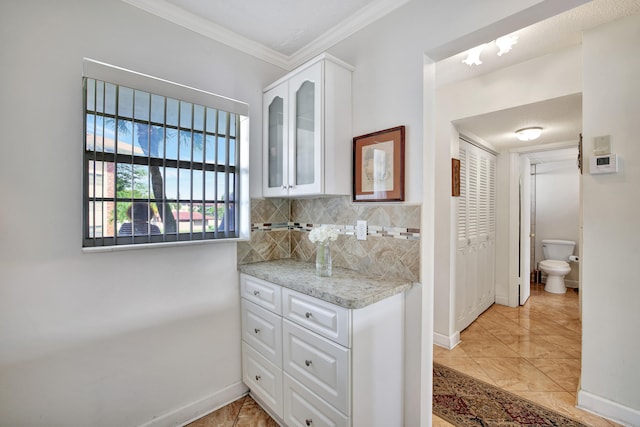 bathroom featuring tile patterned flooring, tasteful backsplash, crown molding, vanity, and toilet