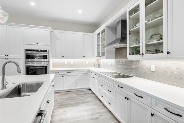 kitchen with sink, wall chimney range hood, white cabinetry, appliances with stainless steel finishes, and light hardwood / wood-style floors