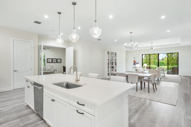 kitchen with decorative light fixtures, a center island with sink, sink, stainless steel dishwasher, and white cabinetry