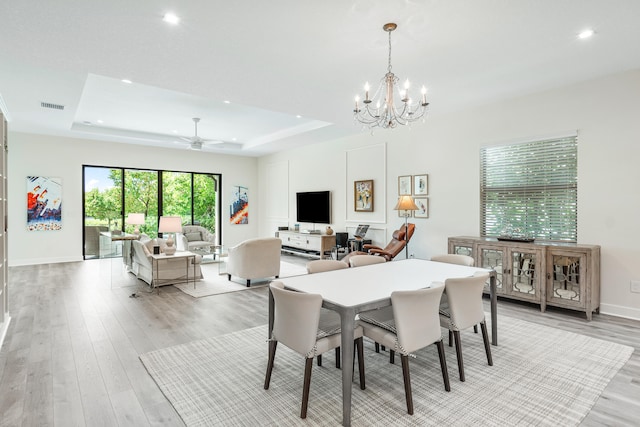 dining area featuring ceiling fan with notable chandelier, light hardwood / wood-style flooring, and a raised ceiling