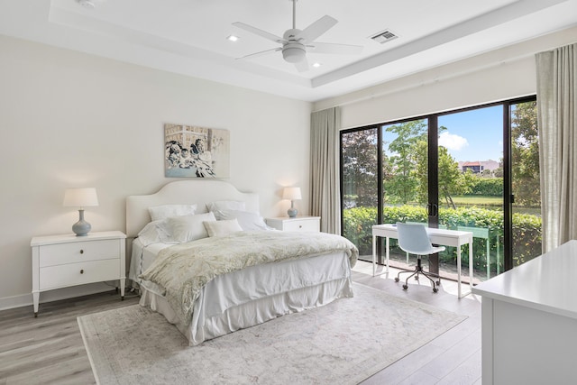 bedroom featuring light hardwood / wood-style floors, a tray ceiling, and ceiling fan