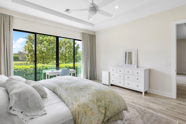 bedroom with access to outside, a tray ceiling, light hardwood / wood-style flooring, and ceiling fan