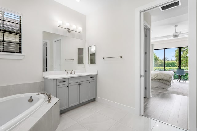 bathroom with ceiling fan, a relaxing tiled tub, tile patterned flooring, and vanity