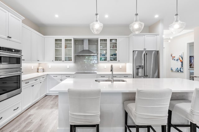 kitchen featuring appliances with stainless steel finishes, wall chimney exhaust hood, sink, and a kitchen breakfast bar