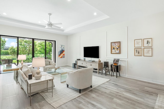 living room with light wood-type flooring, ceiling fan, and a raised ceiling