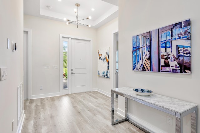 entrance foyer with a raised ceiling, a chandelier, and light hardwood / wood-style flooring