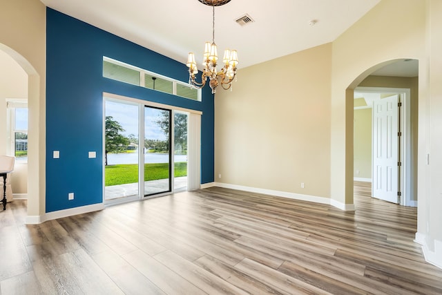 empty room featuring a towering ceiling, hardwood / wood-style flooring, and an inviting chandelier